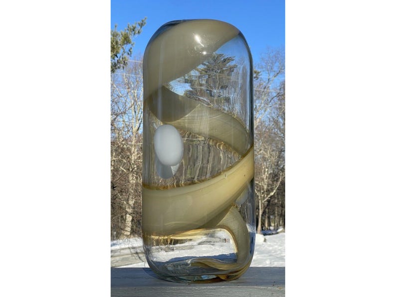May include: A clear glass vase with a swirling pattern of beige and brown glass. The vase has a white orb inside.