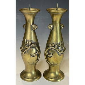 May include: A pair of antique brass candlesticks with intricate floral designs. The candlesticks are tall and slender, with a round base and a flared top.
