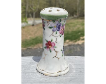 May include: White ceramic bottle stopper with a floral design. The bottle stopper has a green and gold rim and a small hole in the top.