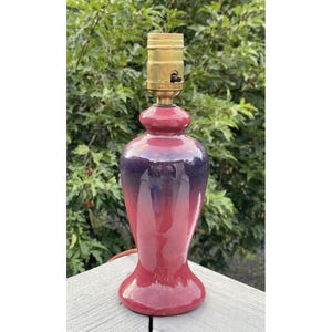 May include: A red and purple ceramic table lamp with a gold metal lampshade. The lamp has a gradient design, fading from dark purple to light red.