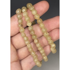 May include: A set of three beaded bracelets. The beads are a light yellow color and appear to be made of a translucent material. The bracelets are strung together on a thin, elastic cord.
