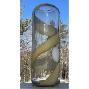 May include: A clear glass vase with a swirling, light brown design. The vase has a round opening at the top and a flat bottom.