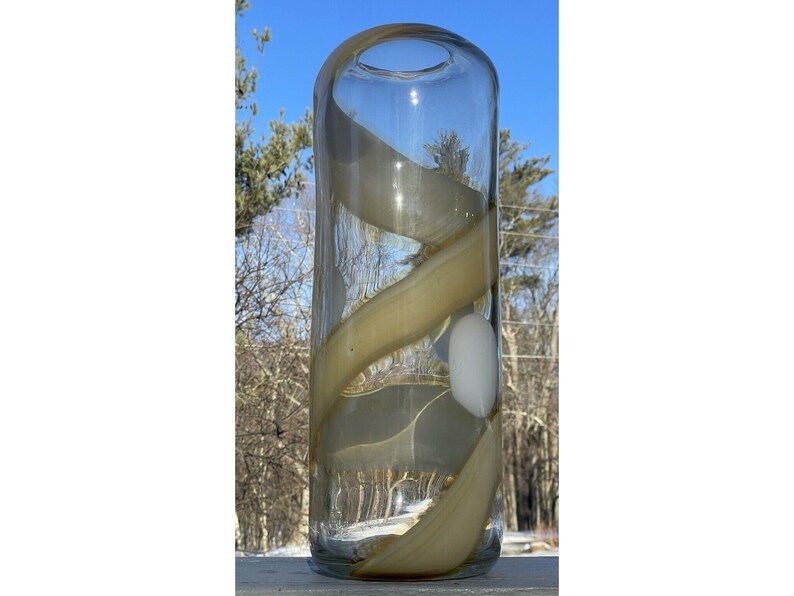 May include: A clear glass vase with a swirling, light brown design. The vase has a round opening at the top and a flat bottom.