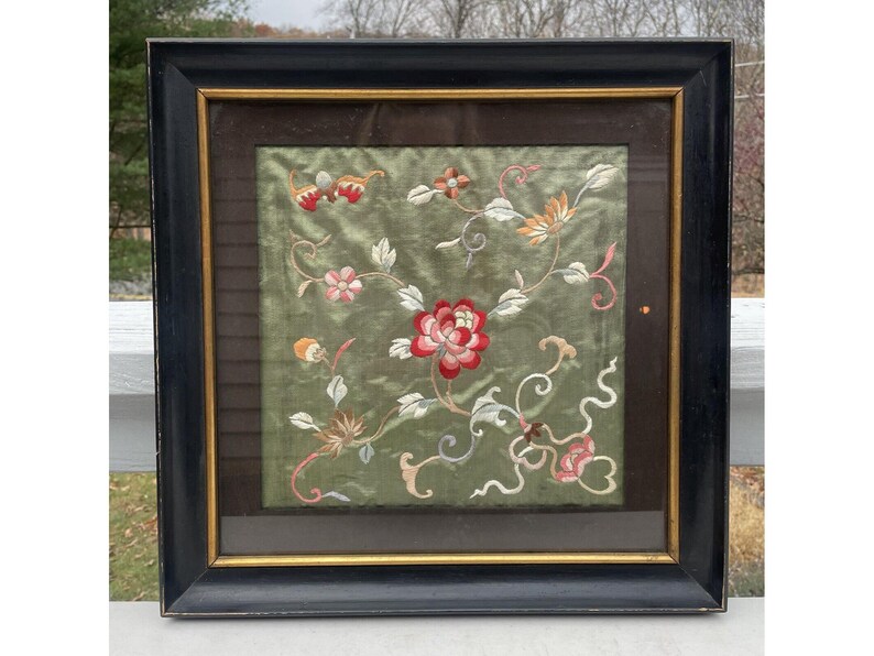 May include: A framed embroidered artwork featuring a floral design with pink, red, and white flowers on a green background. The frame is black with a gold inner border.