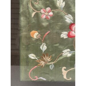 May include: A framed green fabric with embroidered flowers in shades of pink, white, and red. The flowers are arranged in a floral pattern.