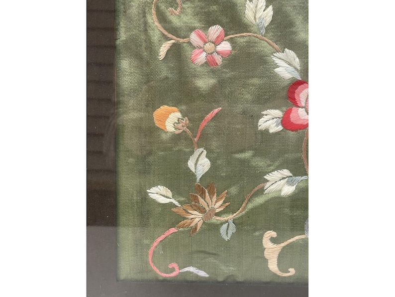 May include: A framed green fabric with embroidered flowers in shades of pink, white, and red. The flowers are arranged in a floral pattern.