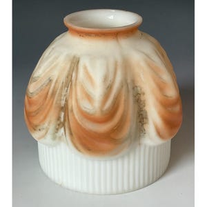 May include: A bell-shaped glass lamp shade featuring a white base with vertical ribbing and a ruffled upper section. The upper portion displays a soft peach-colored gradient with subtle greyish-brown shading within the folds of the glass.