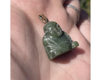 May include: A green jade pendant carved in the shape of a seated Buddha. The pendant has a gold-colored bail for attaching to a chain. The Buddha figure is detailed with carved facial features and clothing.