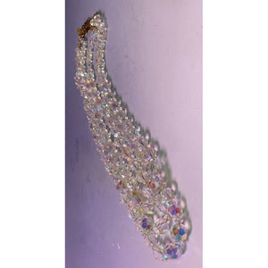 May include: A multi-strand necklace made of iridescent clear glass beads. The necklace is made of several strands of beads that are connected together with a gold clasp.