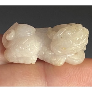 May include: A small, off-white carved figurine of a mythical creature, possibly a Foo Dog or similar guardian figure. The sculpture is detailed with visible features and rests on a hand.
