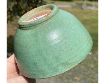 May include: A green ceramic bowl with a speckled glaze. The bowl has a rounded shape and a slightly raised rim. The number "4809" is written on the bottom of the bowl.