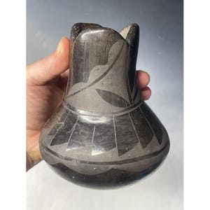 May include: Black pottery vase with a geometric design. The vase has a wide base and a narrow neck.