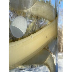 May include: A close-up of a clear glass vase filled with white and yellow glass pieces. The glass pieces are arranged in a spiral pattern. The vase is sitting on a white surface.