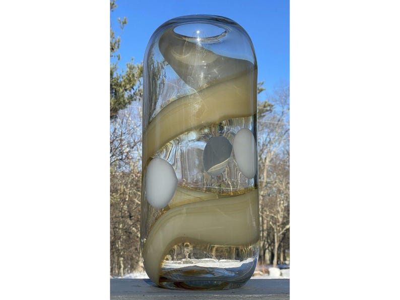 May include: A clear glass vase with a swirl design in beige and white. The vase has a cylindrical shape and is approximately 10 inches tall.