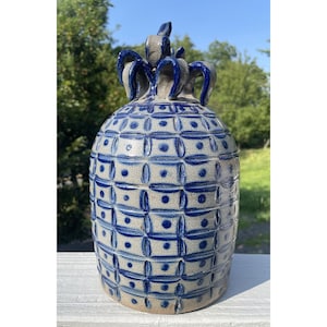 Puede incluir: Una jarra de cerámica gris con un patrón geométrico azul y blanco. La jarra tiene una boca ancha y dos asas.