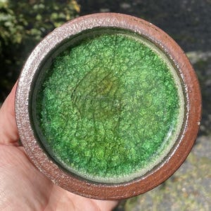 May include: A handmade ceramic bowl with a textured green interior and a brown rim. The bowl's interior has a crackle glaze effect, and the rim is a darker shade of brown. The bowl is round and appears to be a decorative piece.