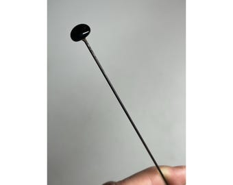 May include: A black glass bead on a thin metal pin. The pin is long and straight.
