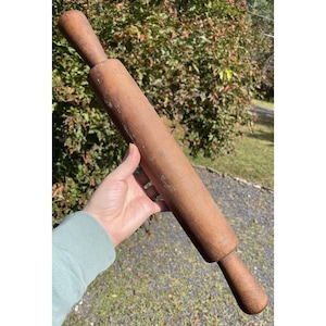 May include: A vintage wooden rolling pin with a cylindrical body and two rounded handles. The rolling pin is a warm brown color, showing signs of wear, suggesting it's been used for baking. The handles are attached to the main body.