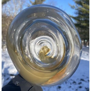 May include: A close-up of a clear glass with a swirling pattern. The glass is filled with a light brown liquid.
