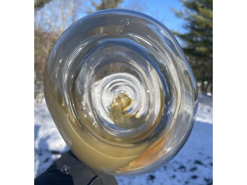 May include: A close-up of a clear glass with a swirling pattern. The glass is filled with a light brown liquid.