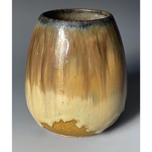 May include: A handmade ceramic vase with a unique, organic shape. The vase features a blend of colors, including shades of brown, yellow, and a touch of blue at the rim. The glaze has a glossy finish, adding to its visual appeal. This decorative piece is suitable for home decor.