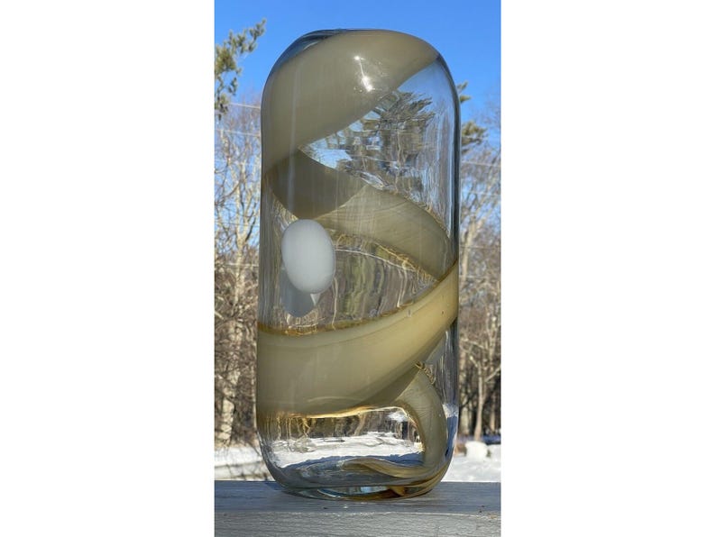 May include: A clear glass vase with a swirling, opaque, cream-colored design. The vase has a round, cylindrical shape.