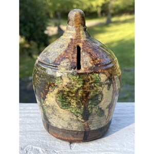 May include: A small, ceramic piggy bank with a brown, green, and white glaze. The piggy bank has a slot on the top for coins.