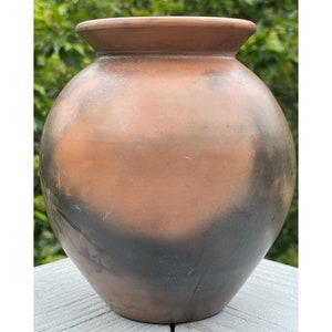 Może przedstawiać: Brązowy i czarny ceramiczny wazon o zaokrąglonym korpusie i lekko rozszerzającym się brzegu.
