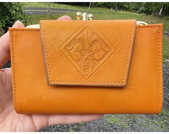 May include: A brown leather wallet with a clasp closure and an embossed floral design. The wallet has a fold-over flap with a stitched edge.
