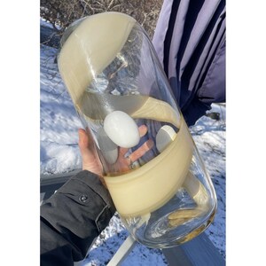 May include: A large, clear glass vase with a swirling, cream-colored design. The vase is filled with a white, round object.