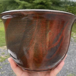 May include: A brown and red ceramic planter with a marbled glaze. The planter is round and has a wide opening.