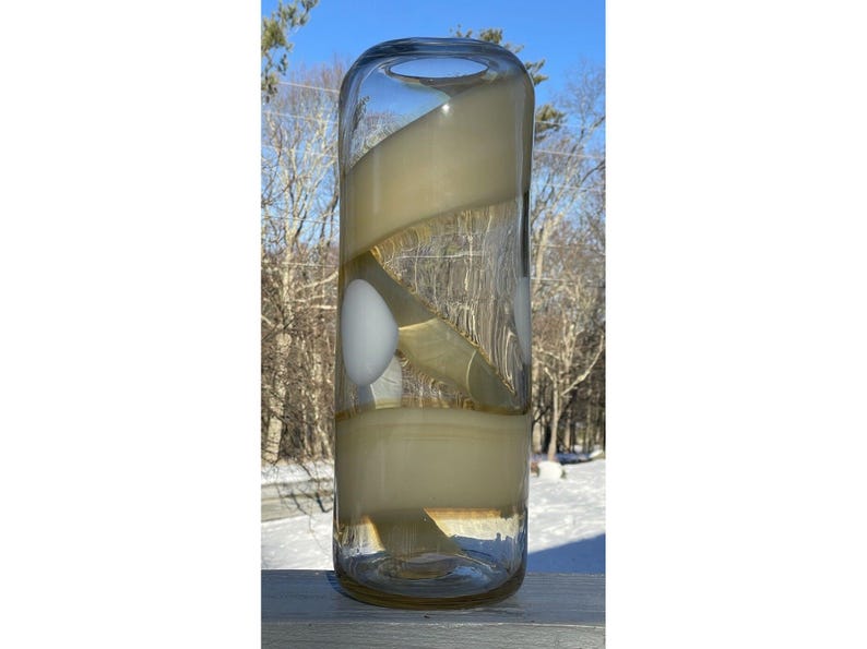 May include: A clear glass vase with a swirling pattern of white and yellow glass. The vase is cylindrical in shape and has a wide mouth.