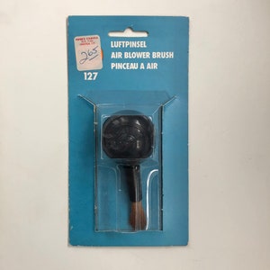 May include: A black air blower brush with a brown bristle brush on a blue and white package. The package says "Luftpinsel Air Blower Brush Pinceau a Air" and has the number 127 on it.