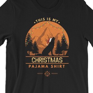 May include: Black t-shirt with a graphic of a wolf wearing a Santa hat in a forest scene. The text "This is my Christmas Pajama Shirt" is printed on the shirt.