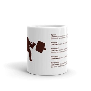 May include: White ceramic mug with a brown silhouette of a Sasquatch lifting a barbell. The mug has a definition of the word "Sasquatch" and its variations, including "Sasquatchy" and "Sass-quat".