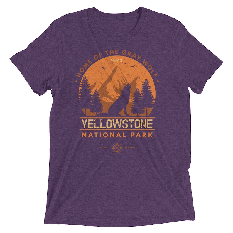 May include: Purple t-shirt with a vintage-style graphic of a wolf howling at the moon in front of a mountain range. The graphic says "Home of the Gray Wolf, Yellowstone National Park, 1872".