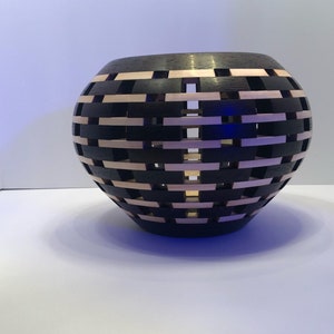 May include: A black and white wooden bowl with a geometric pattern. The bowl is made of thin strips of wood that are woven together to create a lattice design.
