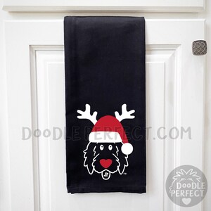 Pu&ograve; includere: Asciugamano da cucina nero con un doodle bianco di un cane che indossa un cappello di Babbo Natale rosso e corna di renna. Il testo "Doodle Perfect.com" &egrave; stampato sull'asciugamano.