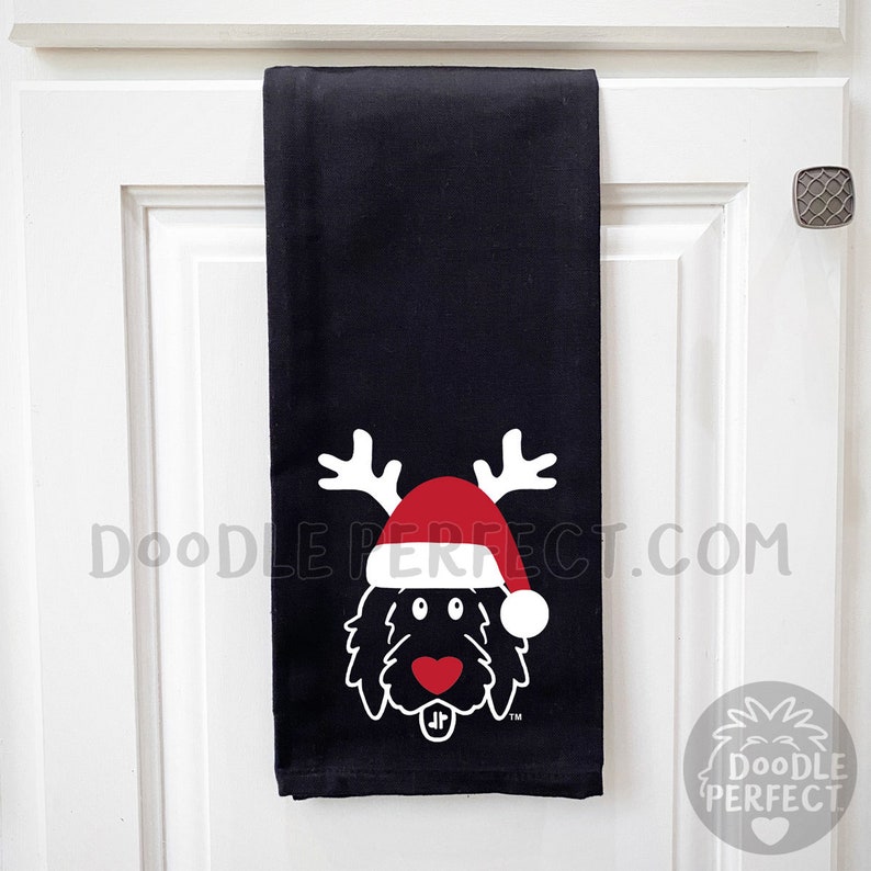 Pu&ograve; includere: Asciugamano da cucina nero con un doodle bianco di un cane che indossa un cappello di Babbo Natale rosso e corna di renna. Il testo "Doodle Perfect.com" &egrave; stampato sull'asciugamano.