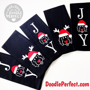 Pu&ograve; includere: Set di cinque asciugamani da cucina neri con lettere bianche che compongono la parola "JOY" e un doodle di un cane con un cappello di Babbo Natale e corna di renna. Gli asciugamani sono piegati e disposti a ventaglio.