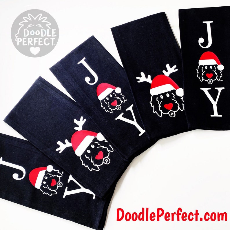 Pu&ograve; includere: Set di cinque asciugamani da cucina neri con lettere bianche che compongono la parola "JOY" e un doodle di un cane con un cappello di Babbo Natale e corna di renna. Gli asciugamani sono piegati e disposti a ventaglio.
