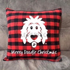 May include: Red and black buffalo plaid pillow with a white doodle dog graphic and the text "Merry Doodle Christmas". The pillow is square-shaped and has a soft, textured appearance.