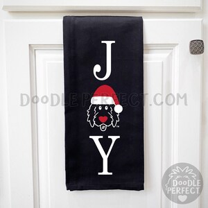 Pu&ograve; includere: Asciugamano da cucina nero con la parola "JOY" in lettere bianche. La "O" &egrave; sostituita da un doodle di un cane che indossa un cappello rosso da Babbo Natale.