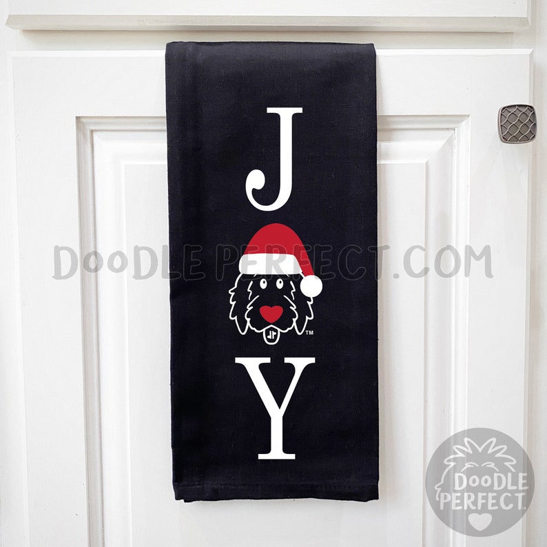 Pu&ograve; includere: Asciugamano da cucina nero con la parola "JOY" in lettere bianche. La "O" &egrave; sostituita da un doodle di un cane che indossa un cappello rosso da Babbo Natale.