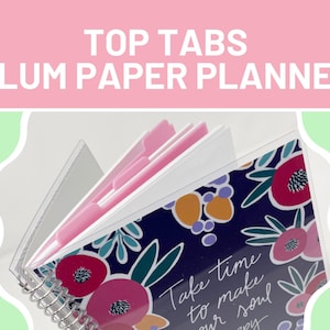 Può includere: Un'agenda rilegata a spirale con linguette superiori rosa e un design floreale. La copertina è blu navy con fiori colorati e il testo "Take time to make your soul happy". Lo striscione in alto recita "TOP TABS PLUM PAPER PLANNER".