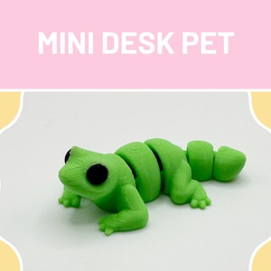 Peut inclure: Une figurine de grenouille verte segmentée imprimée en 3D. La grenouille a de grands yeux noirs et une surface texturée. La figurine est un animal de compagnie de bureau.