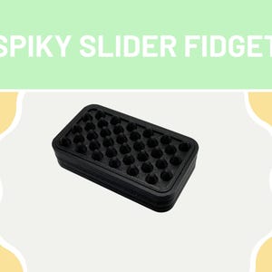 May include: A rectangular black fidget toy featuring a grid of small, pointed spikes on its top surface. The object is labeled with the text SPIKY SLIDER FIDGET in white letters against a light green background at the top of the image.