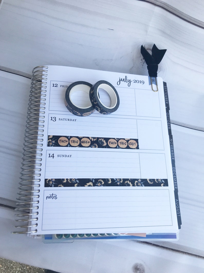 May include: A close-up of a July 2019 calendar page with a black and white floral patterned washi tape and a black washi tape with the text "FUCK THIS WEEK" and "FUCK THIS SHIT" on it.