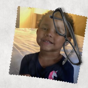 May include: Black rectangular eyeglasses with clear lenses. The glasses are positioned over a smiling child wearing a navy blue shirt with a unicorn graphic. The image is set against a soft, textured background.