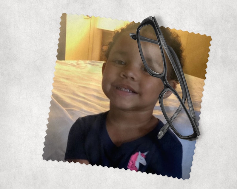 May include: Black rectangular eyeglasses with clear lenses. The glasses are positioned over a smiling child wearing a navy blue shirt with a unicorn graphic. The image is set against a soft, textured background.